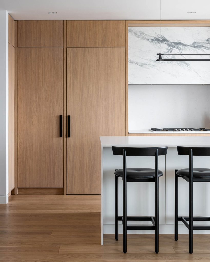 A light wood pantry in a sleek, white and marble kitchen.