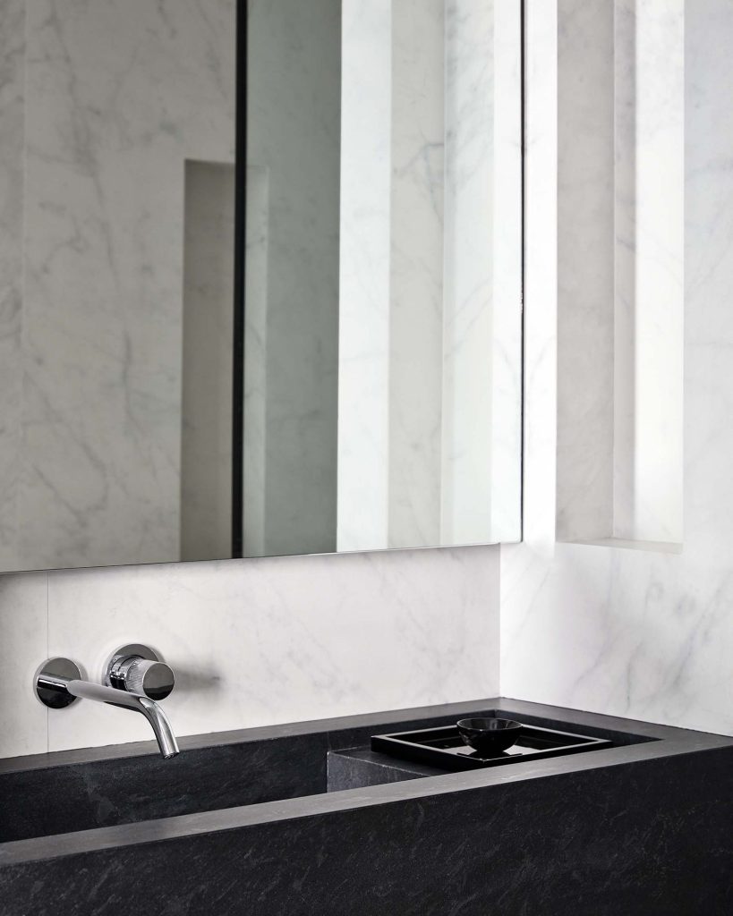 A dark marble sink stands out against white marble walls.